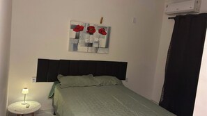 Ein Schlafzimmer mit einem Bett, einer Nachttischlampe, einer Wand-Klimaanlage und einem Gemälde von roten Blumen.