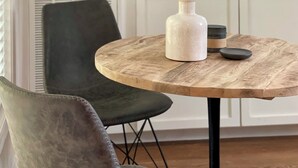 A dining area with a round wooden table, a green upholstered chair, and a white vase. - Secluded 2.5-Acre Retreat: Rustic Charm & Modern Comfort in Land O’ Lakes. (Land O' Lakes)