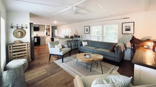 A spacious living area with a sofa, chairs, a coffee table, and a kitchen in the background. - Secluded 2.5-Acre Retreat: Rustic Charm & Modern Comfort in Land O’ Lakes. (Land O' Lakes)
