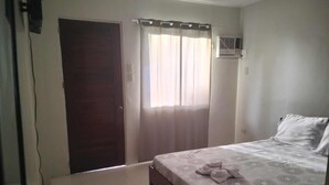 Un dormitorio con cama, ventana con cortinas, puerta y unidad de aire acondicionado.