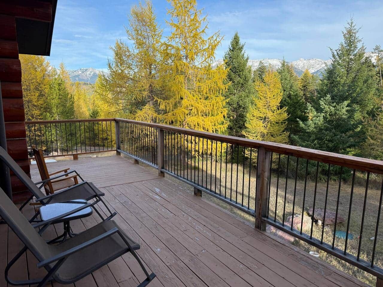 Una terraza de madera con barandilla metálica, dos sillones de descanso y vistas a árboles y montañas.