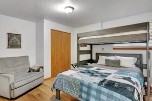 Une chambre avec un lit superposé, un canapé, une porte en bois et un tableau encadré au mur.