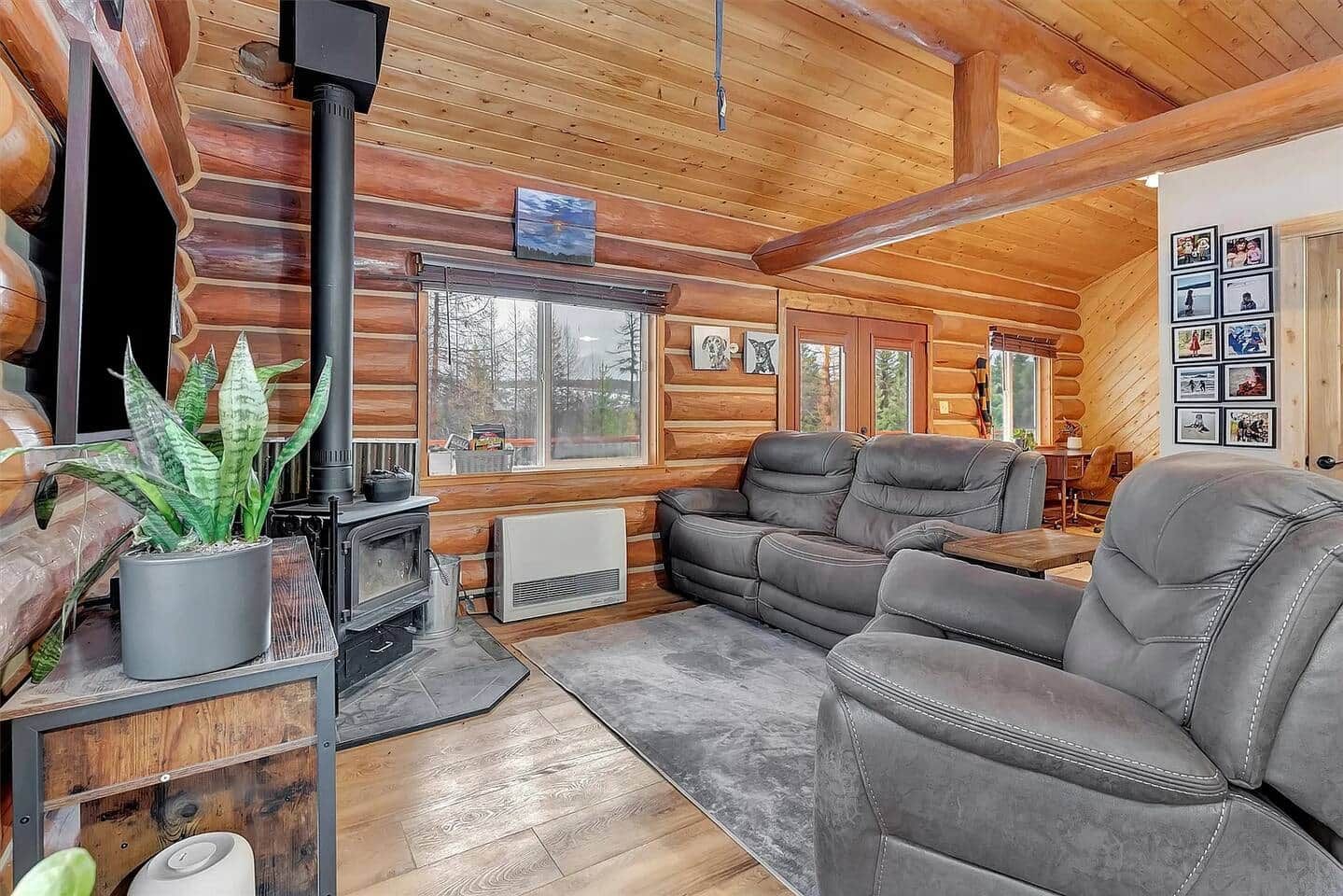 A log cabin interior with a fireplace, leather sofa, and a large window.