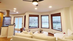 Uma sala de estar ampla com ventilador de teto, janelas grandes, área de cozinha e um espaço de estar aconchegante.