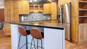 Uma cozinha moderna com armários de madeira, eletrodomésticos de aço inoxidável e uma ilha central com banquetas.