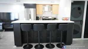 Une cuisine moderne dotée d’un îlot central, de quatre tabourets de bar, d’appareils électroménagers en acier inoxydable et d’armoires en bois.