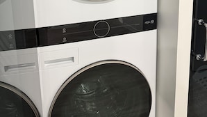 Vue de face d’une buanderie moderne, avec deux machines à laver superposées, un sèche-linge et un panneau de commande.