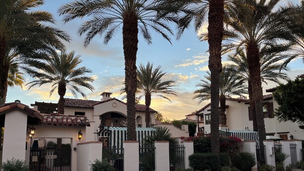 A gated residential area with palm trees, a tiled roof, and a clear sky.