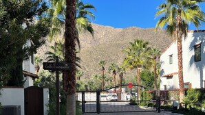 A gated entrance with a sign reading "Calle Tranquilla," palm trees, and a mountainous backdrop.