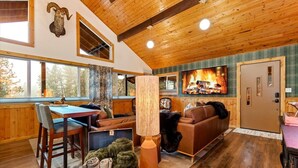 A cozy cabin interior with a dining area, a fireplace, and a large window overlooking a forest. - Remodeled Cabin: Golf & Hot Springs (Garden Valley)