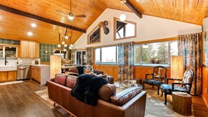 A spacious living area with a brown leather sofa, wooden flooring, and a large window with curtains. - Remodeled Cabin: Golf & Hot Springs (Garden Valley)