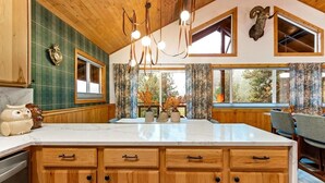 A kitchen with wooden cabinets, a marble countertop, and a large window with curtains. - Remodeled Cabin: Golf & Hot Springs (Garden Valley)