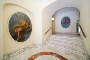 A grand staircase with marble steps and classical paintings on the walls.