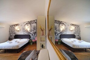 Habitación con espejos, dos camas y un estante central decorado con objetos, además de una pared con estampado de hojas tropicales.