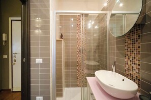 Un baño moderno con ducha de vidrio, un lavamanos blanco y un espejo.