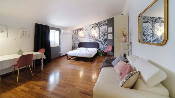 Ett modernt hotellrum med en säng, en soffa, en matplats med stolar och en stor spegel.