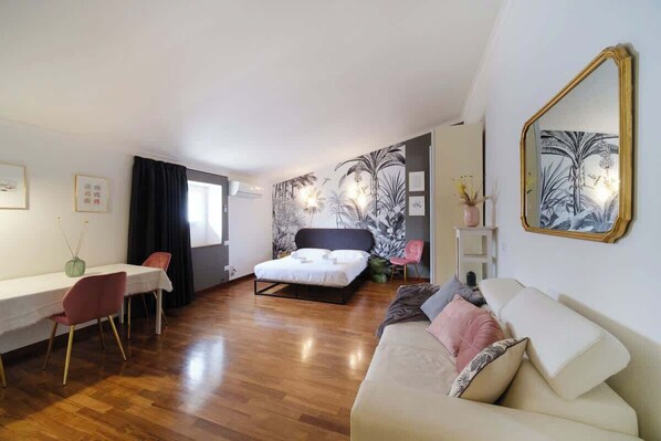 Habitación de hotel moderna con una cama, un sofá, un comedor con sillas y un espejo grande.