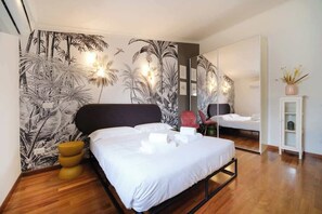 A modern hotel room with a large bed, a mirror, a small seating area, and a wall with a tropical leaf pattern.