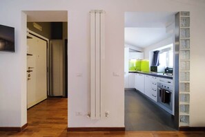A hallway leading to a kitchen with a radiator, a door, and a tiled backsplash.