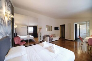 Una habitación de hotel con una cama grande, una zona de estar con sofá y sillones, una mesa de comedor y un espejo.