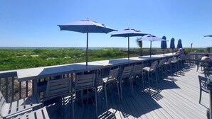 A deck with outdoor seating and umbrellas, overlooking a beach.