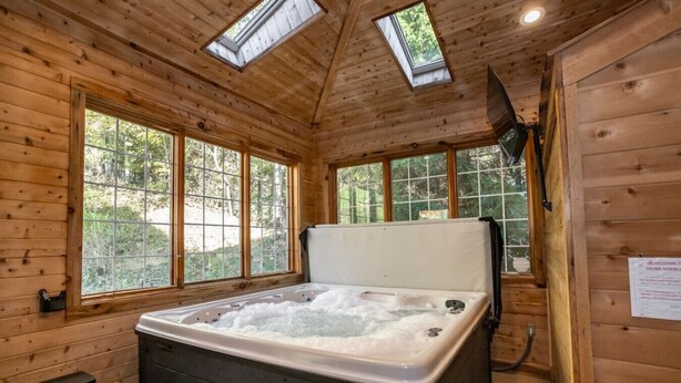 Una cabaña de madera con jacuzzi, ventanas grandes y tragaluces.