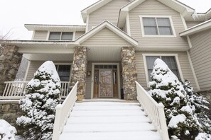 A two-story house with a stone column, a front door, and a staircase leading to the entrance.