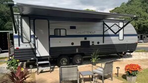 A Grey Wolf RV with a covered living area, a small patio with outdoor furniture, and a garden with potted plants. - The GreyWolf - Convenient & Cozy RV (Mobile)