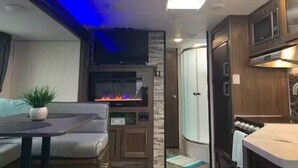 A compact RV interior with a seating area, a fireplace, a kitchenette, and a shower. - The GreyWolf - Convenient & Cozy RV (Mobile)