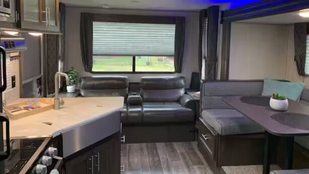 A compact RV interior with a kitchenette, a seating area, and a window providing a view of the outdoors. - The GreyWolf - Convenient & Cozy RV (Mobile)