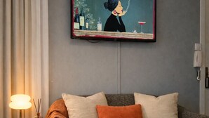 Moderni olohuone, jossa on harmaa sohva, kehystetty taideteos, pieni sivupöytä lampun kanssa ja puulattia.
