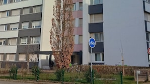 Kerrostalo, jossa on useita kerroksia, parvekkeita, pyöräparkkipaikkoja osoittava kyltti ja jalankulkijoiden käytävä.