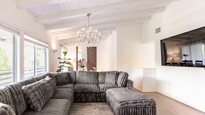 A modern living room with a large sectional sofa, a chandelier, and a large window providing natural light. - Hillside Hideaway - Private Woodland Hills Canyon Guest Suite with Views (Los Angeles)