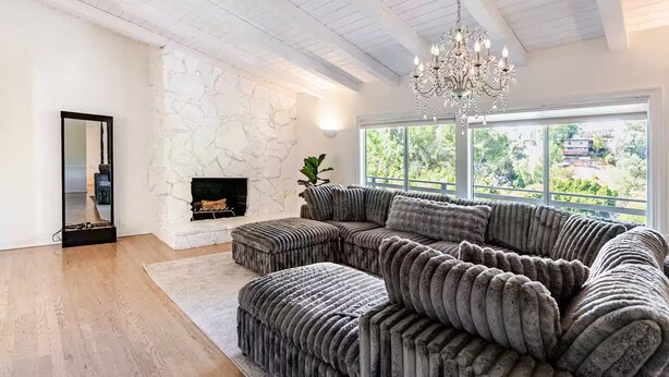 A modern living room with a large sectional sofa, a fireplace, and a large window with a view of greenery. - Hillside Hideaway - Private Woodland Hills Canyon Guest Suite with Views (Los Angeles)
