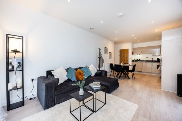 A modern living room with a black sofa, a small coffee table, and a dining area with a table and chairs.