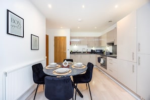 A modern kitchen with white cabinets, a dining area with a round table and black chairs, and framed artwork on the wall.