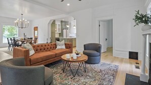 A spacious living room with a brown sofa, a round coffee table, and a grey armchair. A ceiling fan and pendant lights are visible.