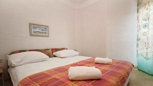 A single-bed room with a plaid bedspread, white pillows, and a framed picture on the wall. - Holiday apartment with air conditioning (Baška)