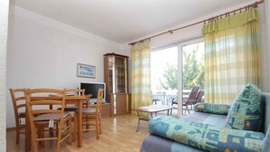 A room with a wooden dining table, chairs, a sofa, a TV, and a cabinet. - Holiday apartment with air conditioning (Baška)