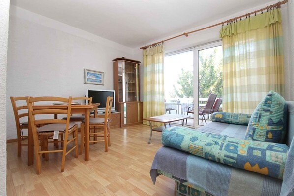 A room with a wooden dining table, chairs, a sofa, a TV, and a cabinet.