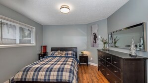 A bedroom with a bed, dresser, nightstand, and a large mirror. - Knockan Hill Rentals - Ground Floor Suite (Victoria)