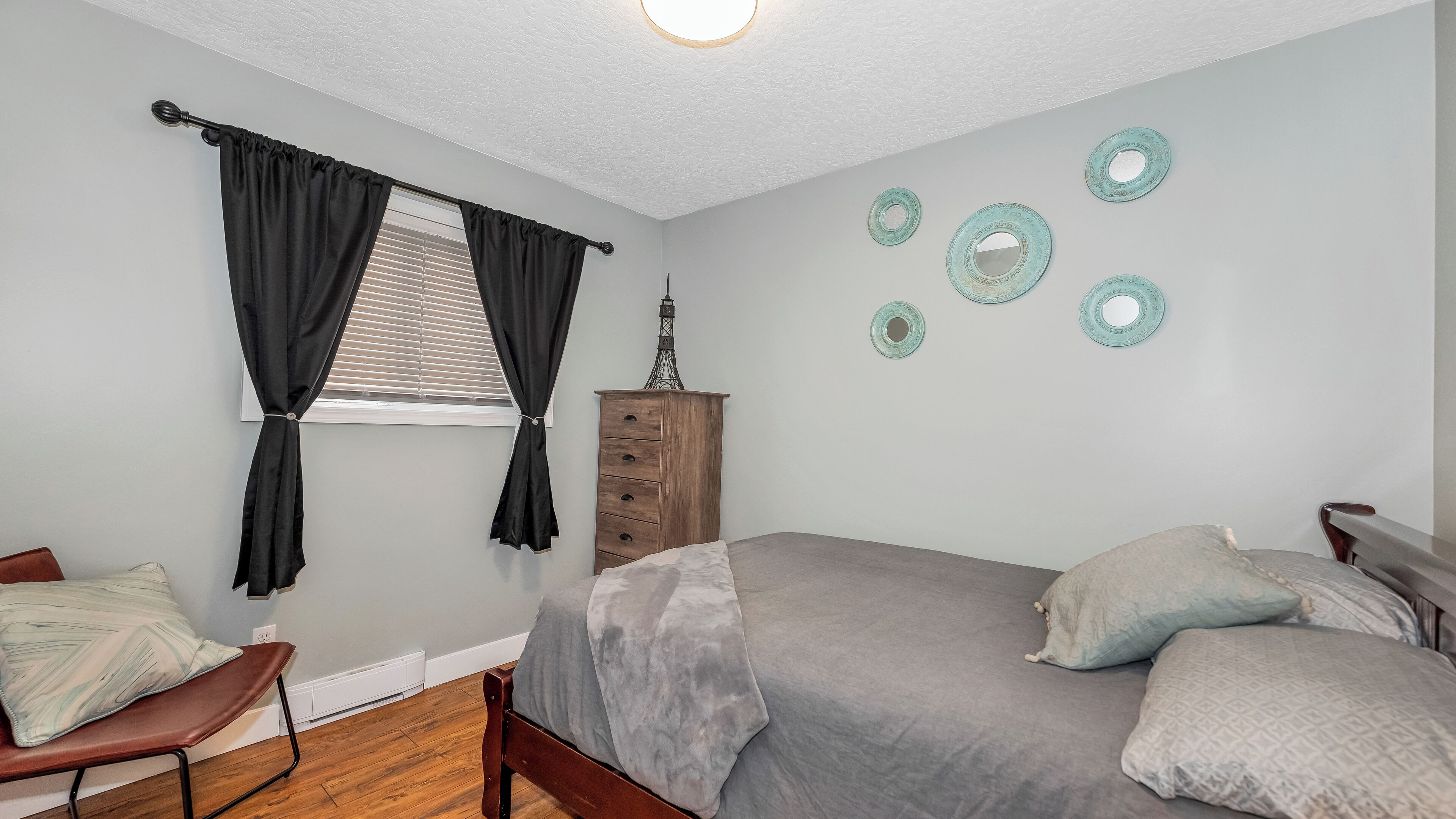 Un dormitorio con cama, cómoda, silla y ventana con cortinas.