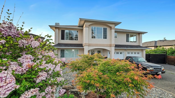 A two-story house with a garage, surrounded by a garden with flowering plants and a driveway with a parked car. - Knockan Hill Rentals - Ground Floor Suite (Victoria)