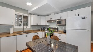 A modern kitchen with white cabinets, a stainless steel sink, a microwave, and a refrigerator. - Knockan Hill Rentals - Ground Floor Suite (Victoria)