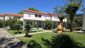 A courtyard with a building featuring a tiled roof, surrounded by greenery and a pathway. - Holiday apartment with terrace near the beach (Baška)
