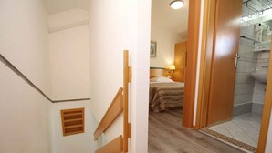 A hotel room with a wooden staircase, a bed with a headboard, a bathroom with a shower, and a small window. - Holiday apartment with terrace near the beach (Baška)
