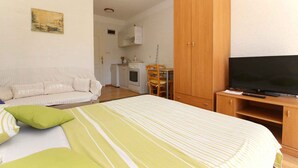 Ein Schlafzimmer mit einem Bett, einem Fernseher, einem Holzschrank und einer Küchenzeile im Hintergrund.