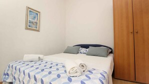 A bedroom with a bed, pillows, a wooden wardrobe, and a framed picture on the wall.