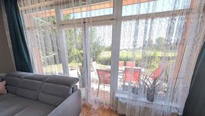 Een woonkamer met een grijze bank, een groene poef en een groot raam met behang.