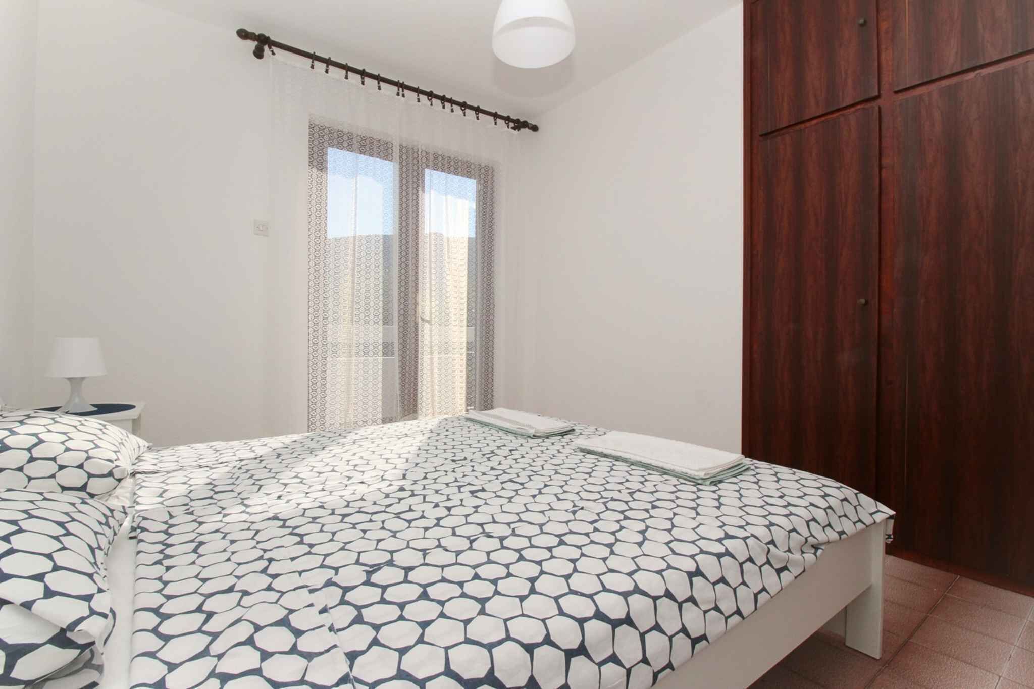 Ein Schlafzimmer mit Bett, Nachttisch, Kleiderschrank und einem Fenster mit gemusterten Vorhängen.